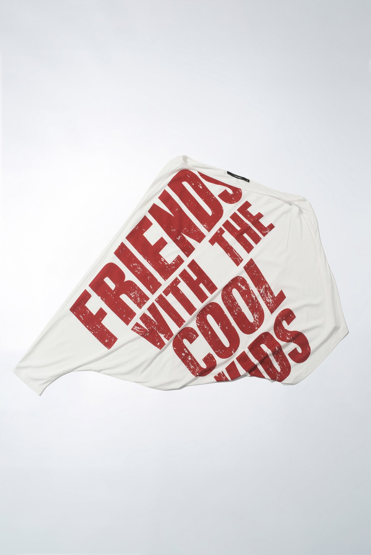 Flat lay of the Eli Top, a white asymmetric one-shoulder top with red slogan print