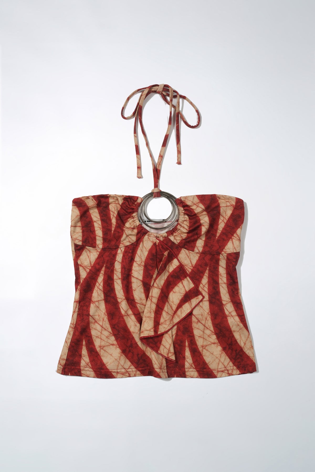 Flat lay of the Zaria Top, a rust red and cream swirl print halter top with silver ring
